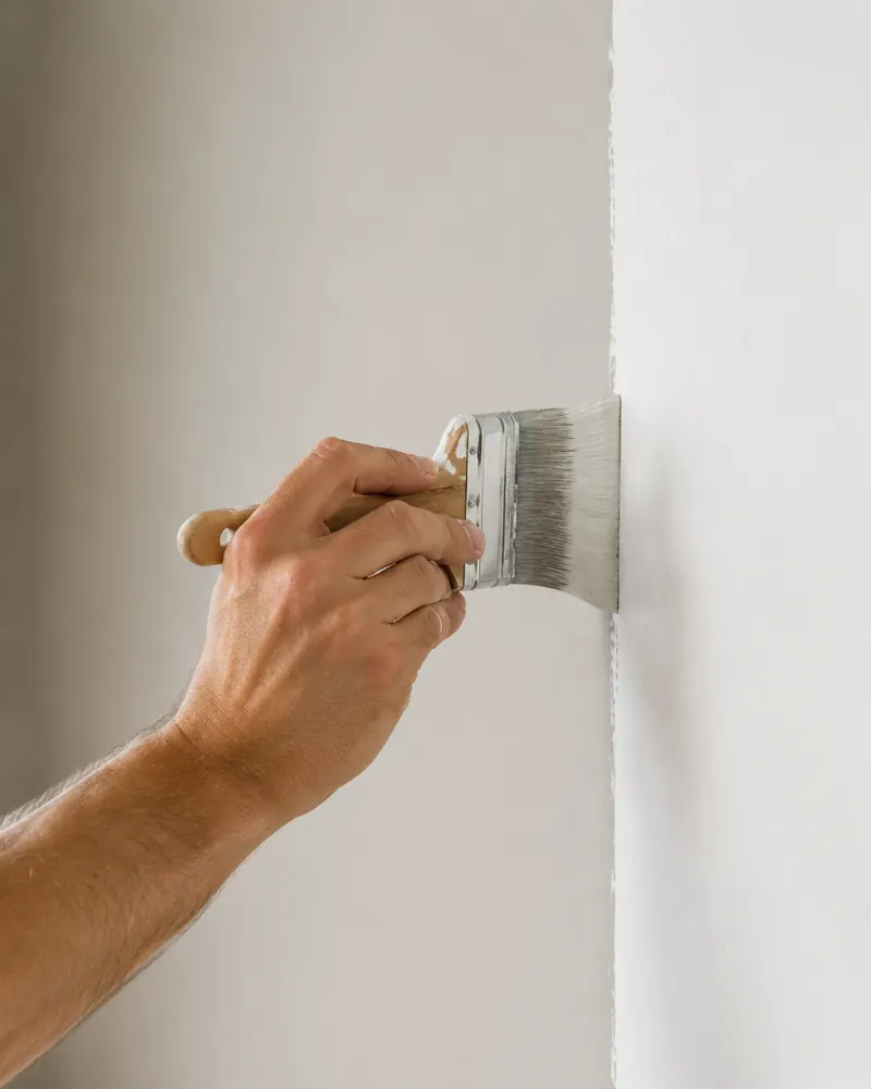 Hand zieht mit dem Flächenstreicher eine gerade Farbkante an einer Innenwand